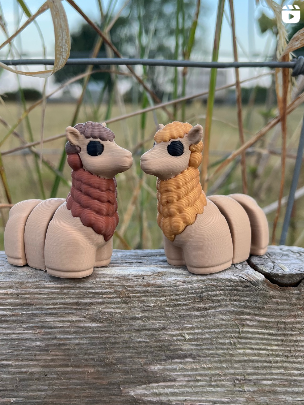 Two toy articulated alpacas on a wooden surface with dry grass in the background