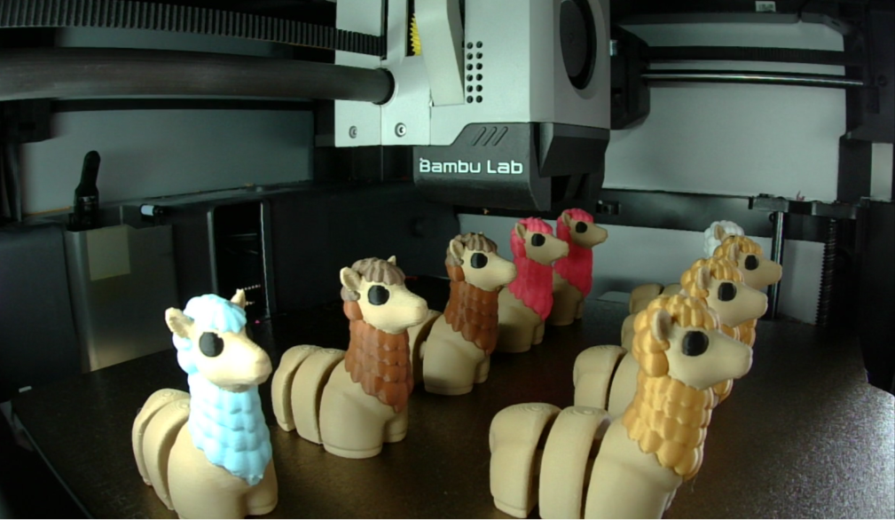 Row of small animal figurines in front of a 3D printer labeled 'Bambu Lab'.