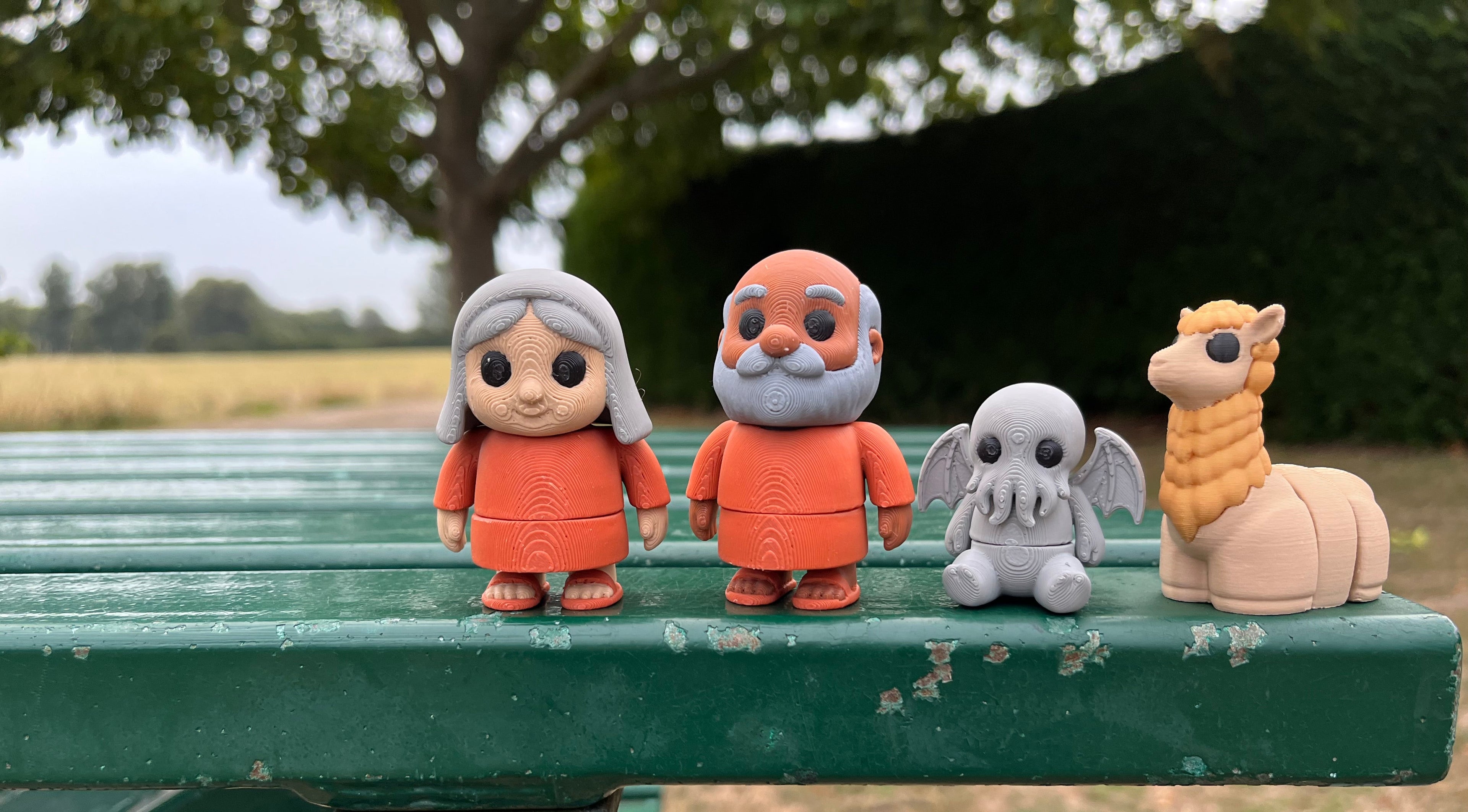 Four articulated fidgets a woman, man, Cthulhu and an alpaca on a green bench with a natural background