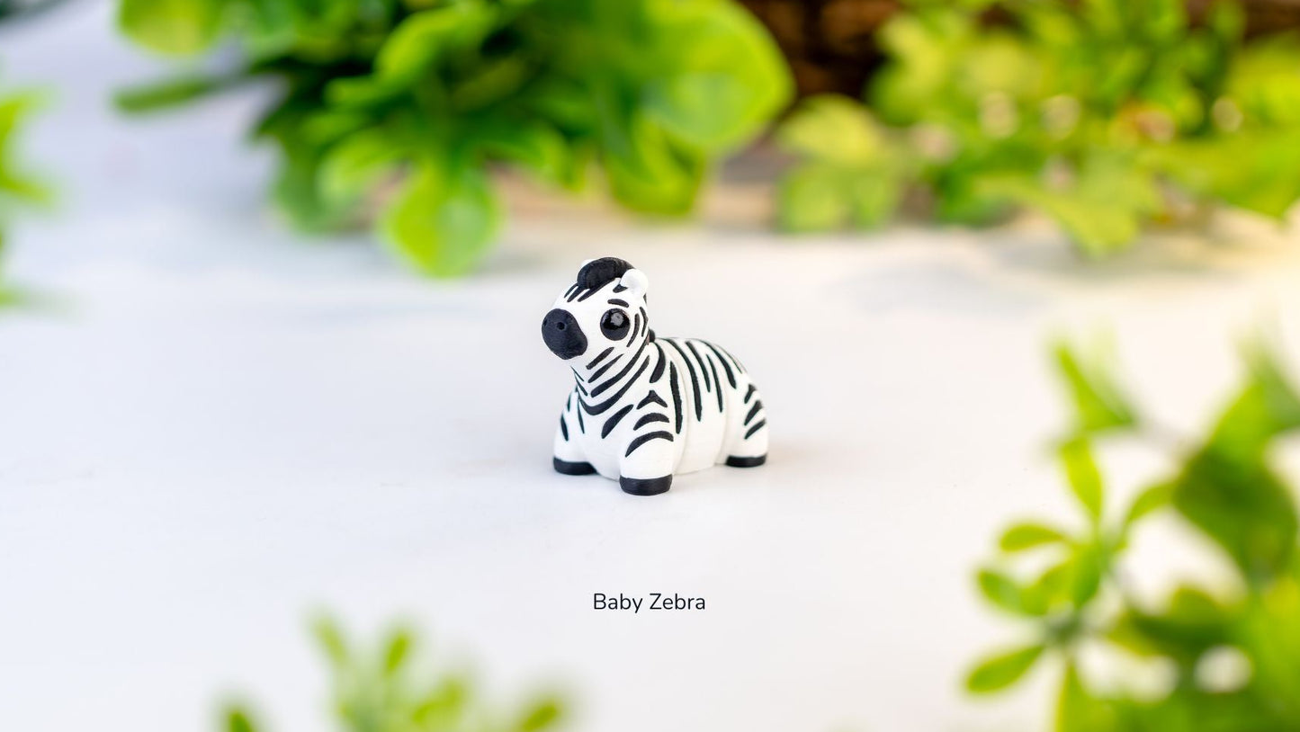 Small zebra figurine on a white surface with green plants in the background