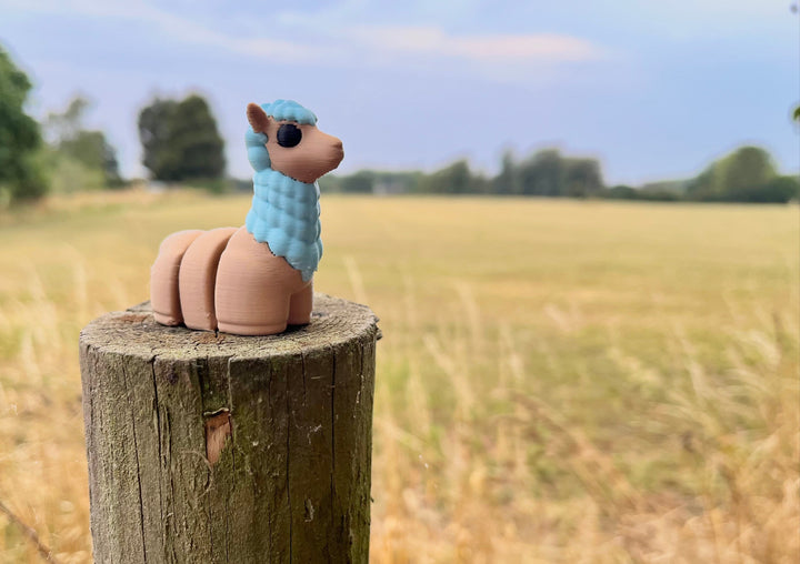 Toy llama with blue on a wooden post with a field and trees in the background