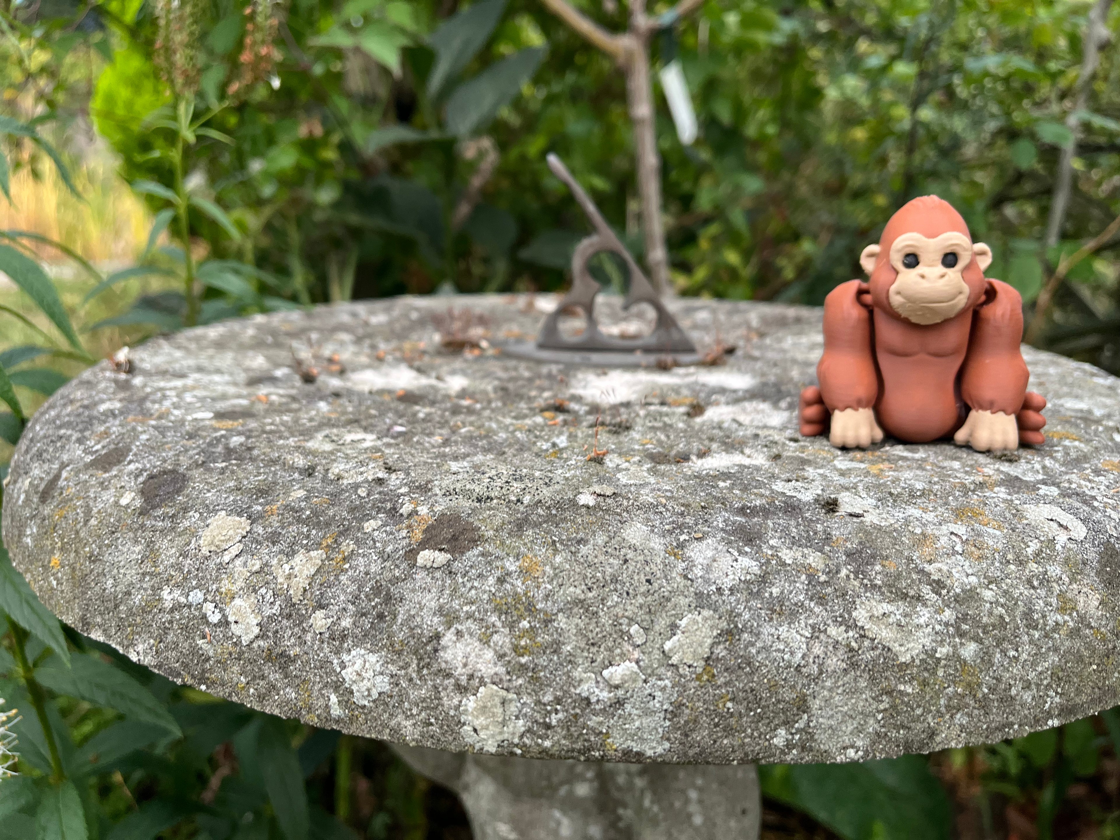 Small brown monkey figurine on a textured stone surface with greenery in the background
