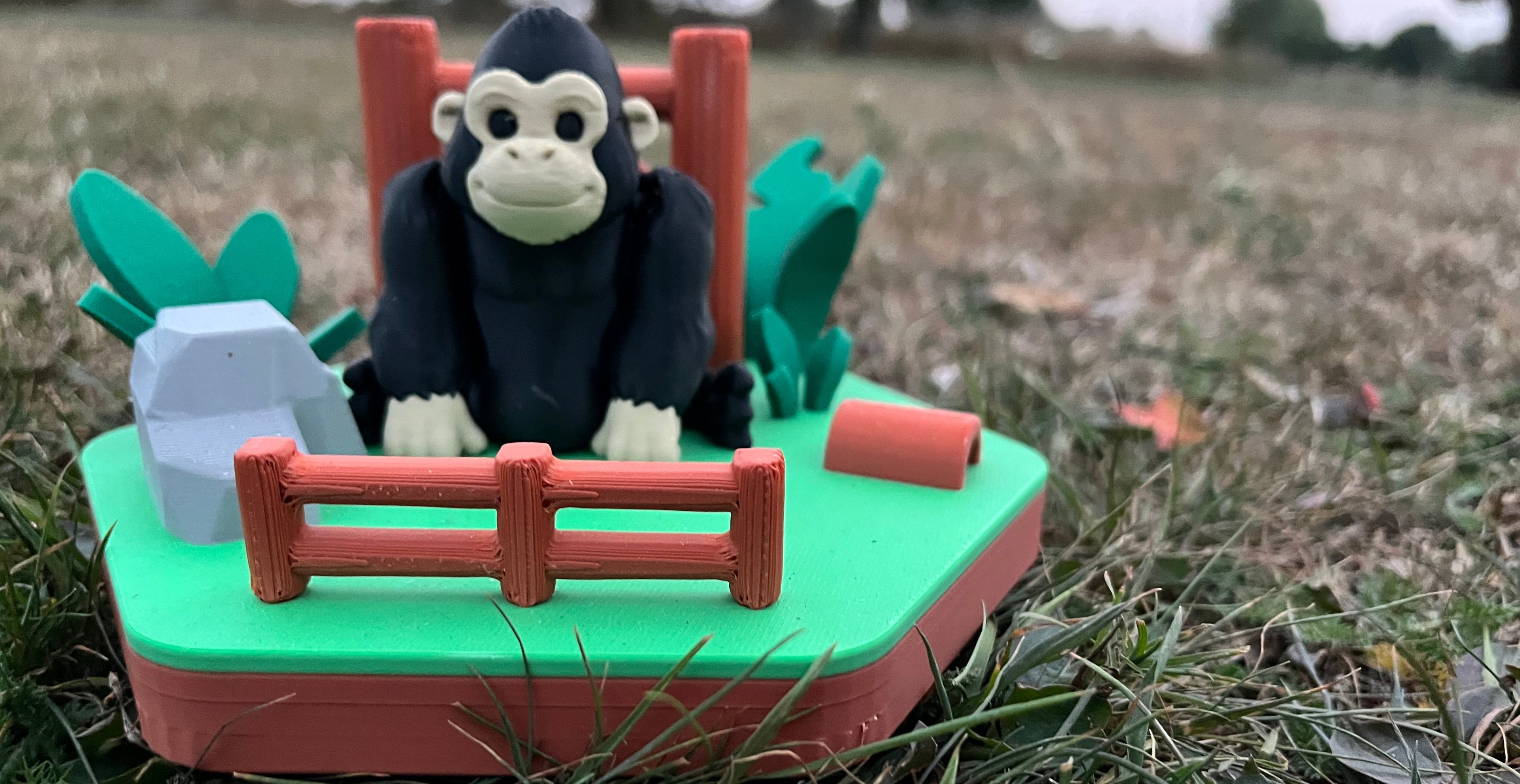 Toy gorilla on a green platform with red railing in a grassy outdoor setting