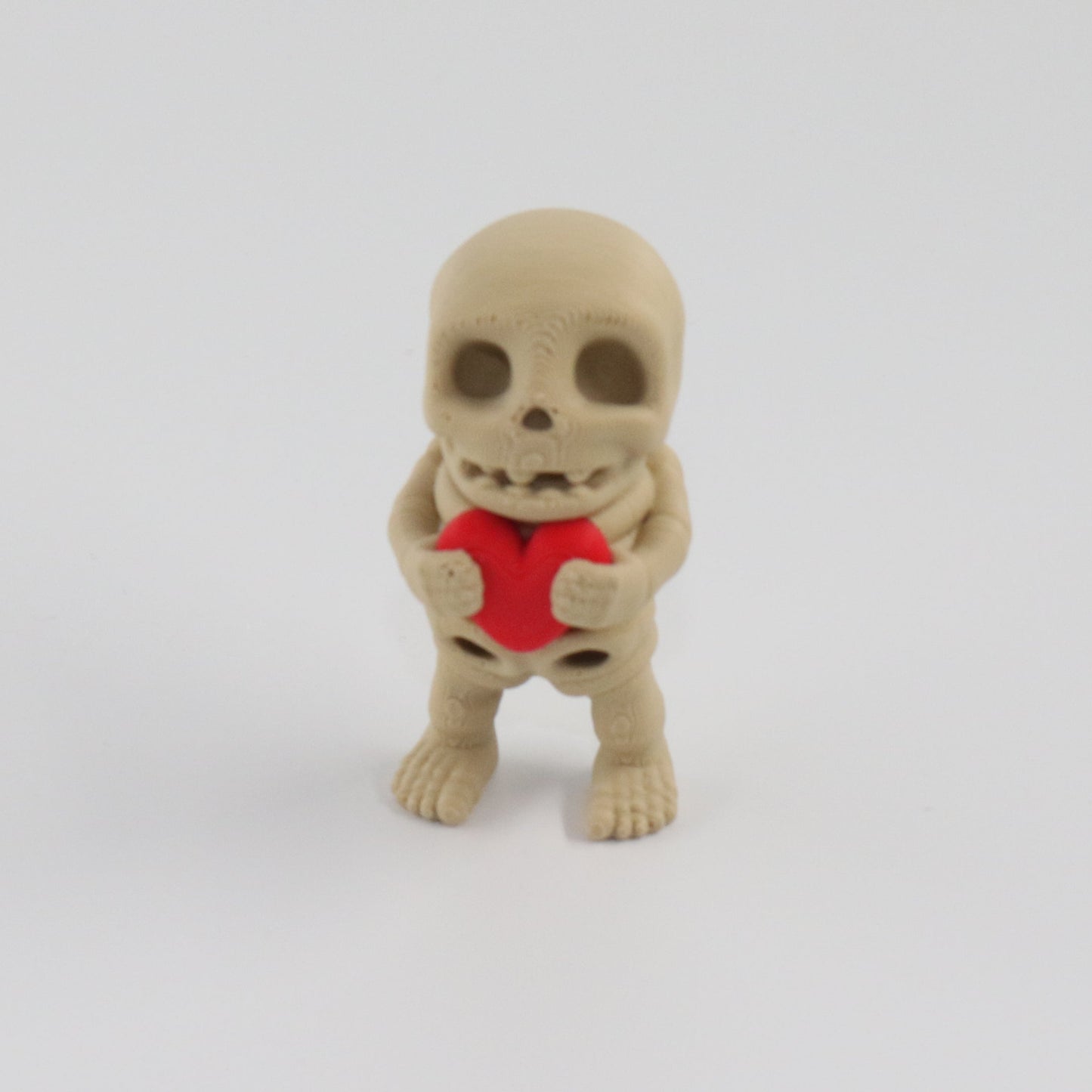 Small skeleton figurine holding a red heart on a white background