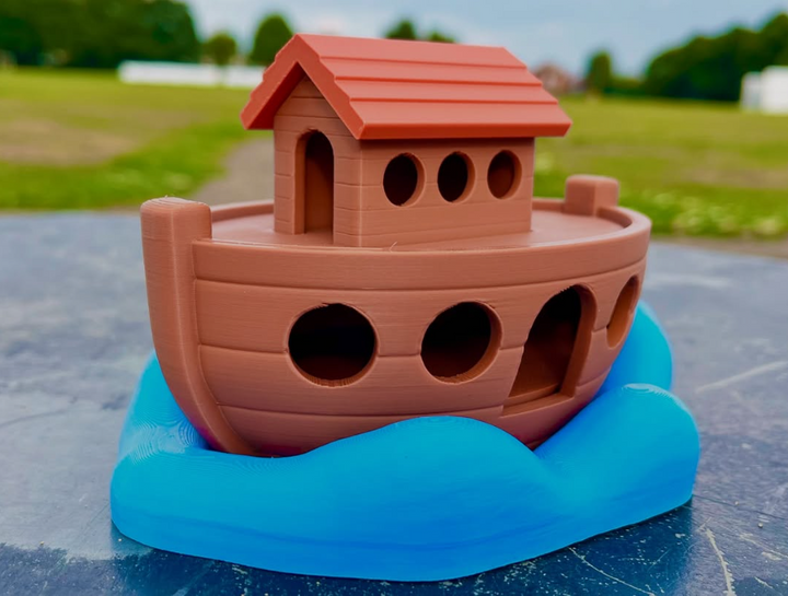 Toy boat with a red roof on a blue wave-shaped base outdoors