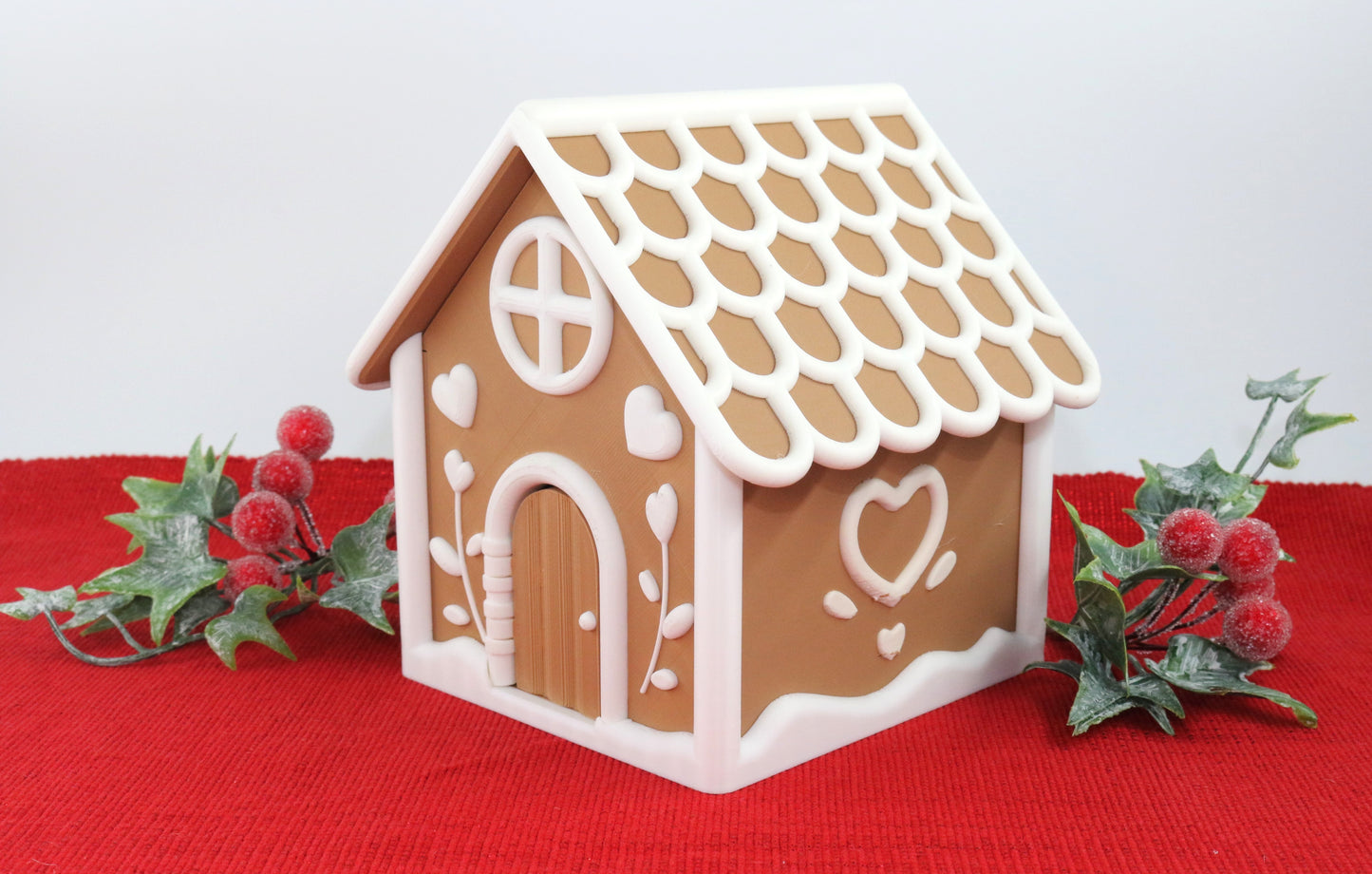Decorative gingerbread house on a red surface with greenery