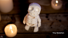 Small skeleton figurine on a wooden surface with a candle and blurred lights in the background.