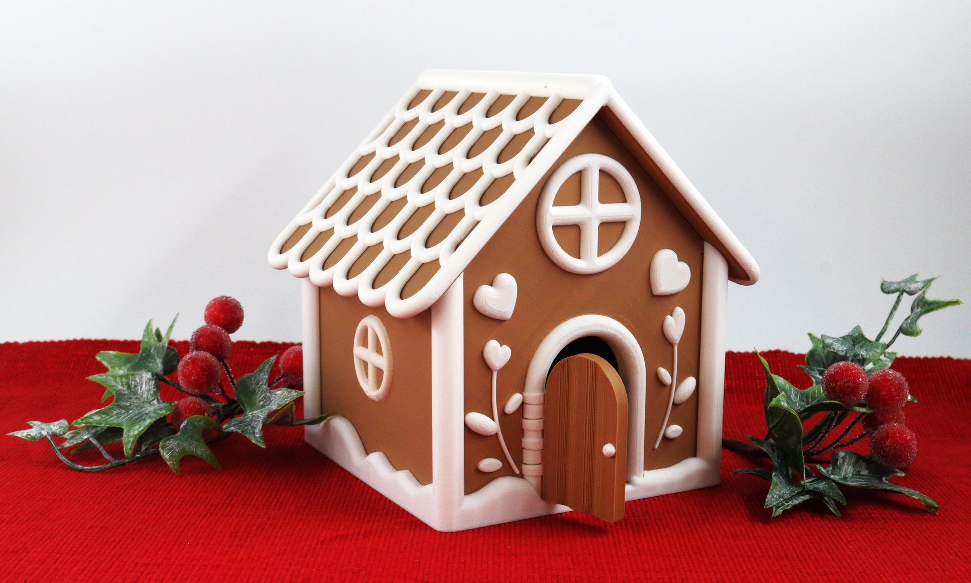 Decorative gingerbread house with a white roof on a red surface with greenery.