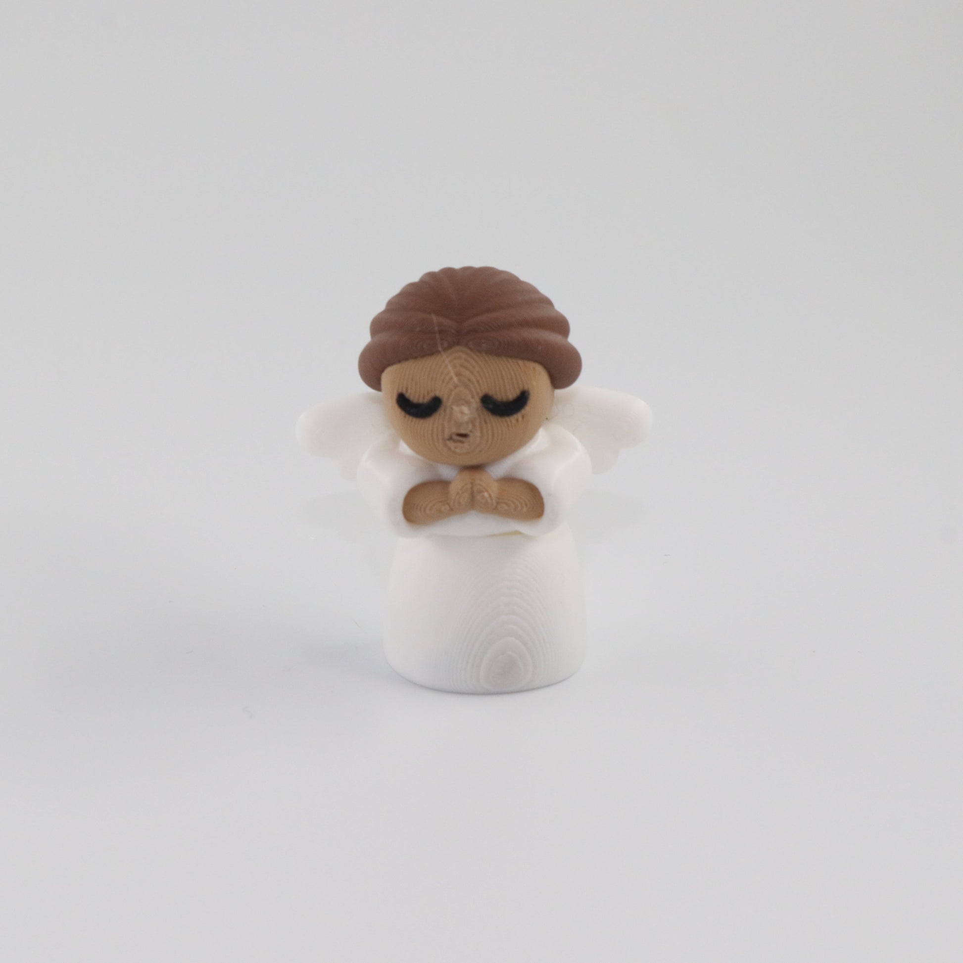 Small figurine of a person with brown hair and a white outfit on a light gray background