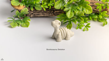 Model of a Brontosaurus skeleton on a white surface with green plants in the background