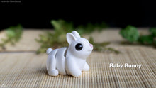White ceramic baby bunny figurine on a woven mat with blurred greenery in the background