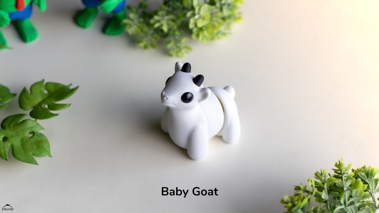 White goat figurine labeled 'Baby Goat' on a light surface with green leaves.