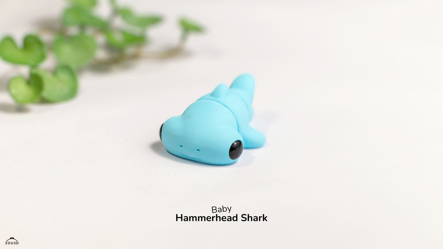 Blue toy hammerhead shark on a white surface with green leaves in the background