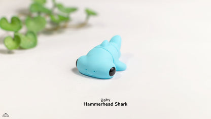 Blue toy hammerhead shark on a white surface with green leaves in the background