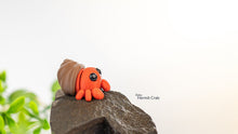 Toy hermit crab on a rock with a blurred plant in the background
