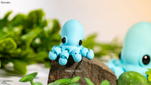 Blue octopus figurine on a rock with green plants in the background