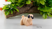 Baby pug figurine on a white surface with greenery in the background