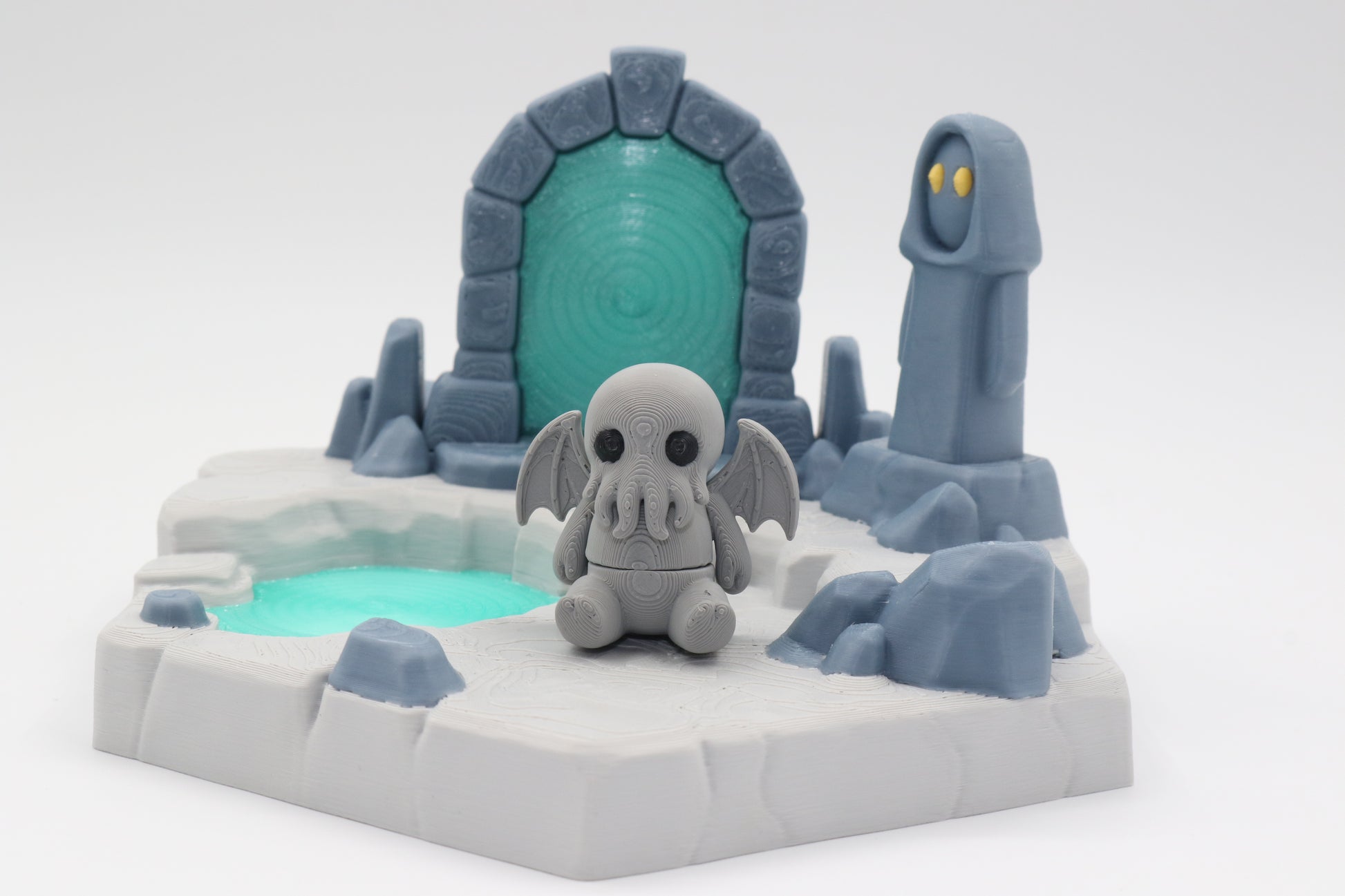A light grey articulated cthulhu and a portal playset with a transparent blue portal and pool of water, and a grey statue spirit
