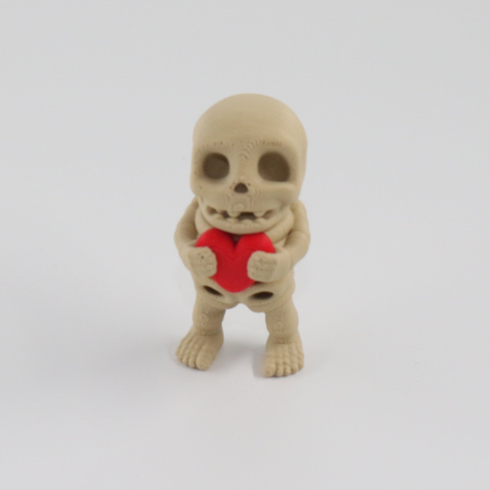 Small skeleton figurine holding a red heart on a white background