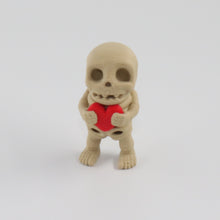 Small skeleton figurine holding a red heart on a white background