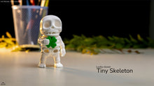 Small skeleton figurine with a green clover, labeled 'Lucky clover Tiny Skeleton', on a blurred background.