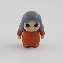 Small figurine with gray hair and brown outfit on a white background