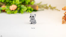 Small gray cat figurine on a white surface with greenery in the background