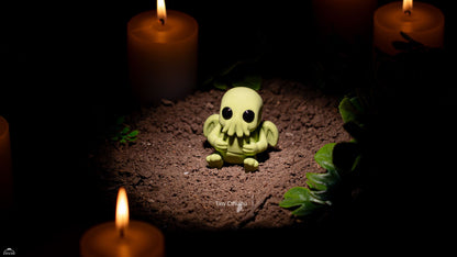 Small green creature figurine on a dark surface with candles around