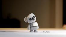 Small gray koala figurine on a reflective surface with a blurred background