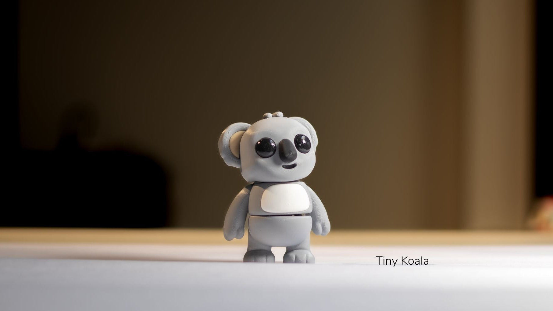 Small gray koala figurine on a light surface with a blurred background