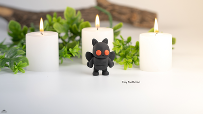 Black creature figurine between three lit candles with greenery in the background
