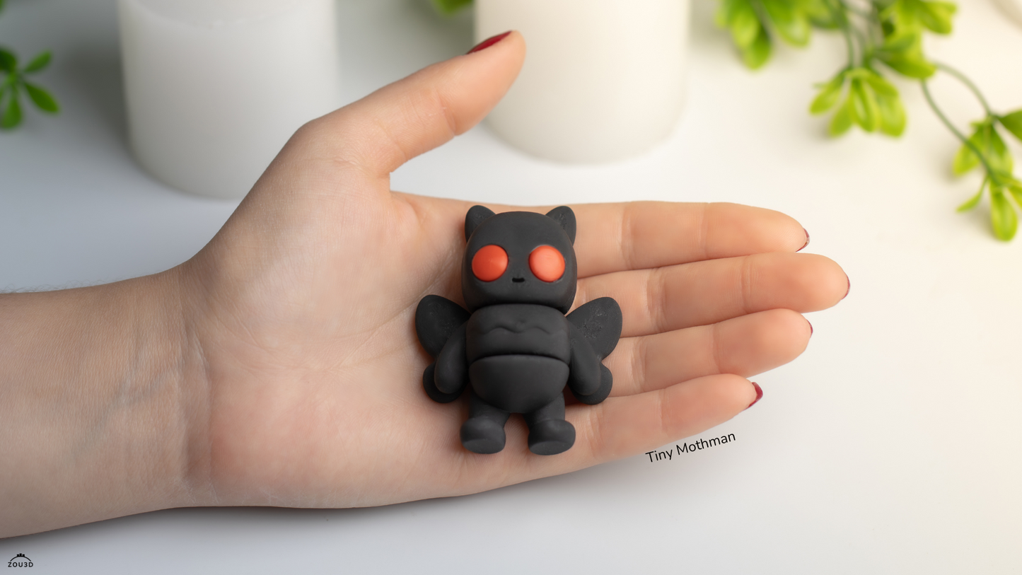 Hand holding a small black creature figurine with red eyes on a light background